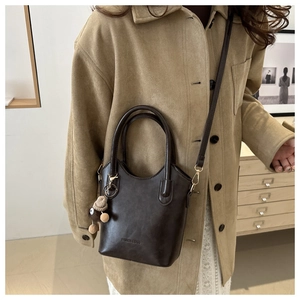 Detail of dark brown leather bucket bag with top handle and plush bear charm decoration