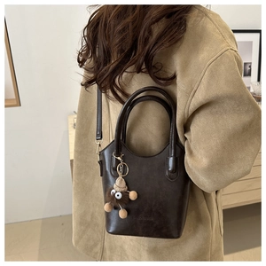 Detail of dark brown leather bucket bag with furry monster charm and fashion logo