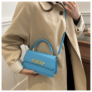 Detail of a bright blue crossbody bag featuring a unique gold bar-shaped metal lock