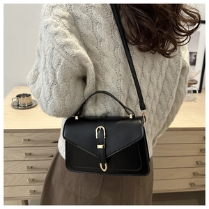 Détail d'un sac bandoulière noir avec rabat en V et boucle dorée sur un pull beige