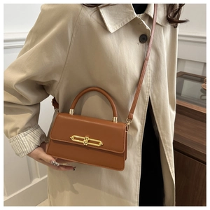 Detail of a brown leather crossbody bag with a gold metal bar lock on a beige trench coat