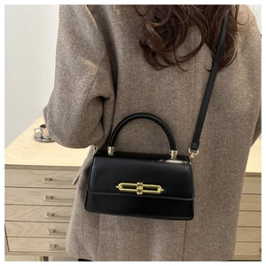 Detail of elegant black glossy leather handbag with gold metal clasp on brown blazer