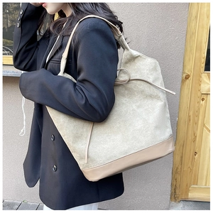 Detail of grey suede tote bag featuring khaki leather handles and side ribbon bow design