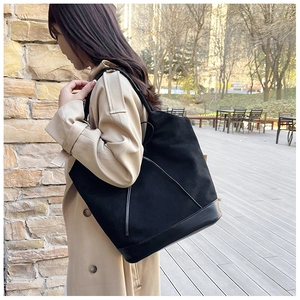 Detail of a black large-capacity tote bag in suede and smooth leather on a model's shoulder