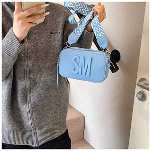 Detail of light blue crossbody bag with embossed SM logo and wide woven strap