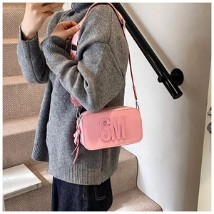Pink crossbody camera bag with wide strap and SM embossed logo in casual setting