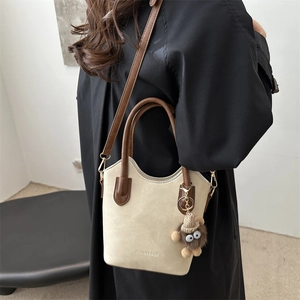 Beige bucket bag with brown handles and plush charm worn by model in black coat