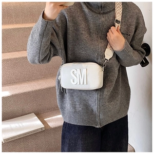 Detail of white leather crossbody bag with SM logo patch and geometric patterned strap
