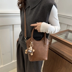 Vintage brown PU leather bucket bag with top handle and plush charm on female model