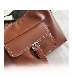 Detailed macro view of brown faux leather bag with contrast stitching and silver buckle