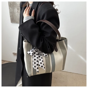 Close-up of striped canvas tote bag featuring a polka dot ribbon bow and leather strap
