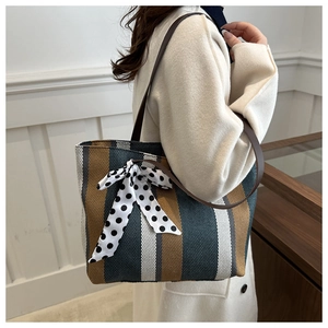 Close-up of large striped tote bag featuring brown leather handles and a polka dot ribbon