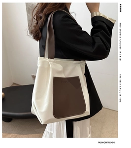 Detail of minimalist beige canvas tote bag featuring a brown leather pocket and long shoulder strap