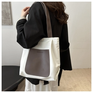 Detail of white tote bag featuring brown front pocket and embossed brand logo on strap