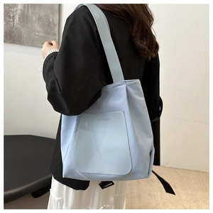 Detail of the light blue tote bag showing the textured brand logo and front pocket stitching