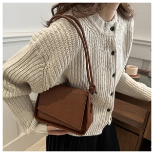Detail of dark brown shoulder bag with woven texture flap and irregular geometric edge