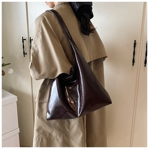 Deep burgundy glossy patent leather tote bag shown on model with minimalist trench coat