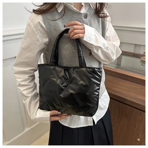 Close-up of black quilted tote bag in shiny nylon fabric held by a model in interior