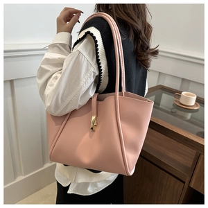 Pink leather tote bag with gold buckle shown on shoulder in a lifestyle setting
