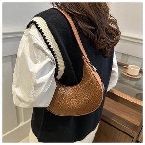 Brown woven crescent underarm bag worn by a model in a cozy indoor lifestyle setting