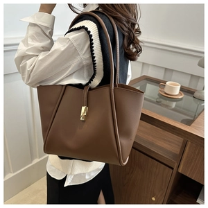 Dettaglio di una borsa tote marrone con fibbia geometrica dorata e tracolla sottile