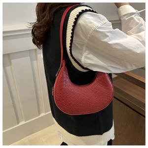Close-up of red crocodile pattern crescent bag worn under the arm by a model