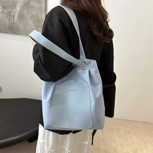 Light blue minimalist nylon tote bag with front pocket shown as stylish shoulder wear