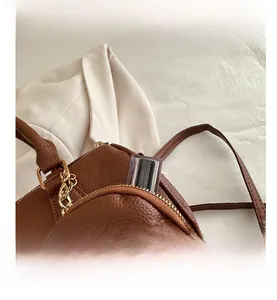 Detail of brown lychee leather handbag featuring gold zipper and round coin purse accessory