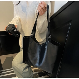 Detail of black oil wax leather tote bag with metal buckle and glossy texture