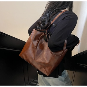 Model wearing a glossy brown tote bag showing its large capacity and shoulder strap detail
