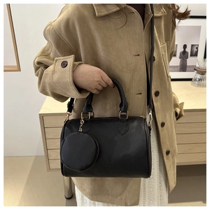 Close-up of black leather Boston bag featuring a round coin purse charm and gold chain detail