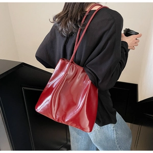 Side view of large red glossy patent leather tote bag with stylish pleated design