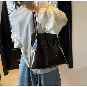 Detail of glossy burgundy leather tote bag with long straps worn by model for daily commute