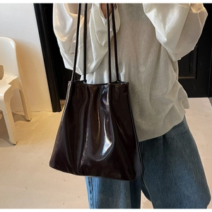 Close-up of a large glossy patent leather bucket bag worn by a model in deep brown