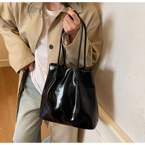 Polished black patent leather tote bag detail held by model in casual beige outfit