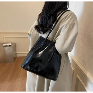 Model wearing a large black patent leather tote bag with a high-gloss finish for daily use
