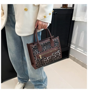 Detail of leopard print tote bag featuring brown leather handles and front zipper pocket