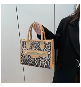 Detail of leopard print handbag with decorative zipper and light brown top handles