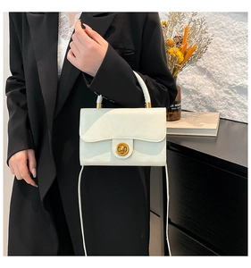 Detail of white square handbag with golden round twist lock and reinforced top handle