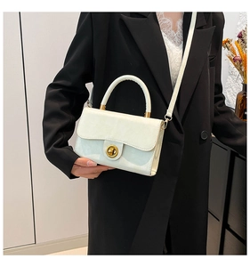 Close-up of a white leather crossbody bag with a gold round twist lock on a black suit