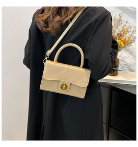 Detailed view of beige faux leather handbag with vintage gold twist lock and handle