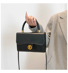 Detail of model holding a black leather flap handbag with a gold round twist lock