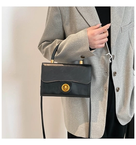 Close-up of a vintage black crossbody bag with a gold metal clasp worn with a grey blazer