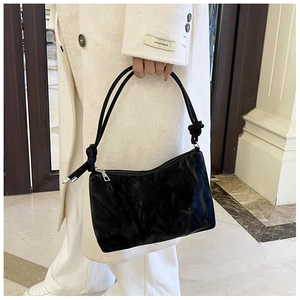 Detail of black underarm bag with knot strap design and premium pleated texture surface