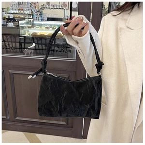 Detail of black pleated shoulder bag with decorative knotted strap and silver metal tips