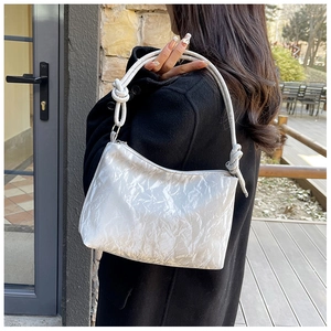 Detail of silver metallic hobo bag featuring knotted shoulder strap and pleated texture