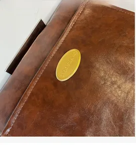 Close-up of vintage brown oil-wax leather texture and golden oval metal brand plate