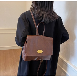 Detail showing vintage dark brown leather backpack texture and gold metal plaque on flap