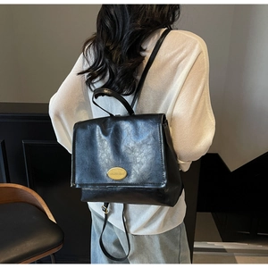 Rear view of a model wearing a black leather backpack with a gold oval plaque detail