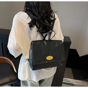 Close-up of black leather backpack featuring a textured flap and gold metal logo plate